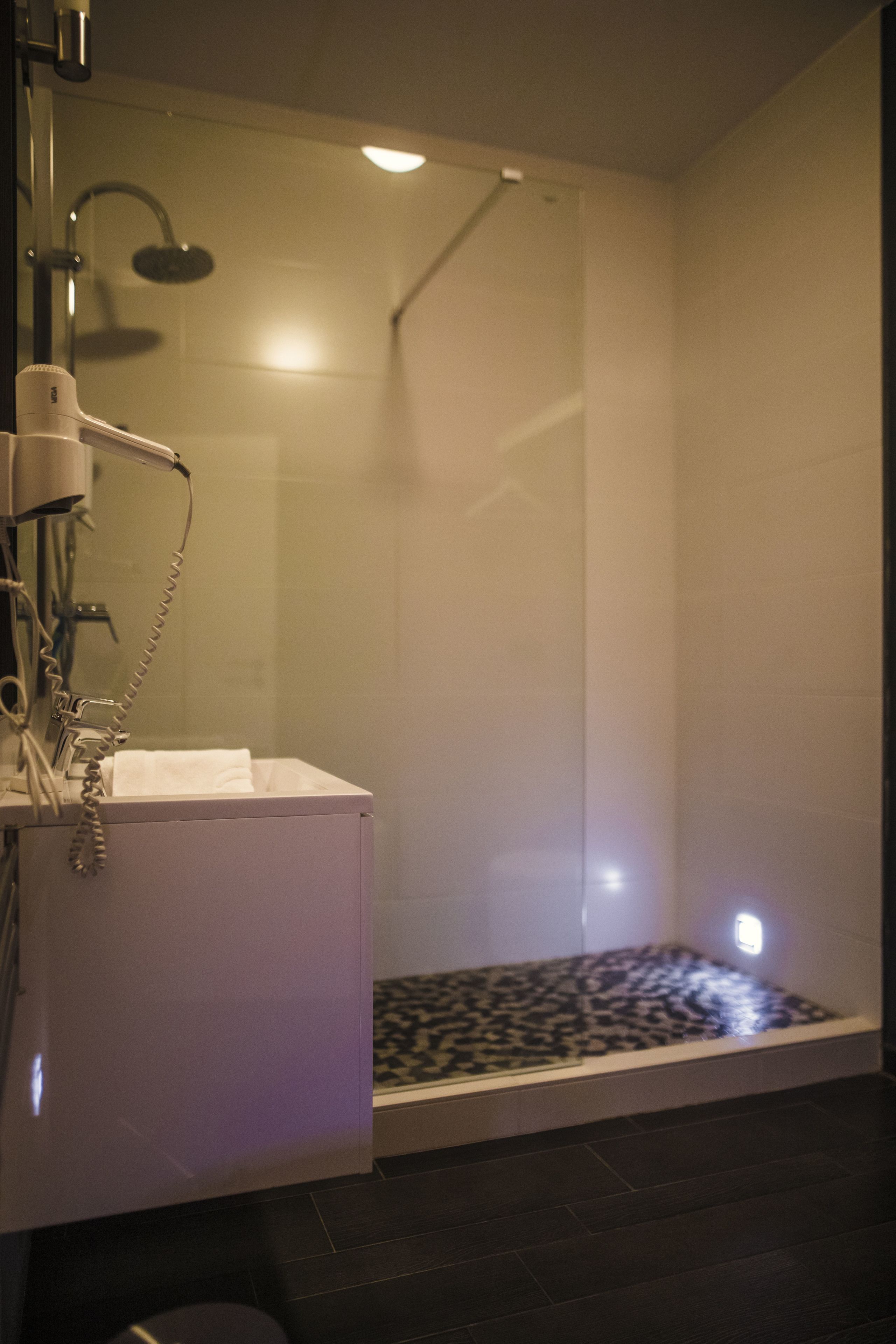 Un bany modern amb una cabina de dutxa de vidre, un lavabo blanc amb una tovallola i un sòl amb dibuixos.