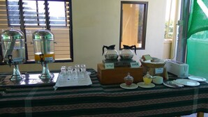 A buffet setup with various food and drink dispensers, a small serving area, and a window with blinds.