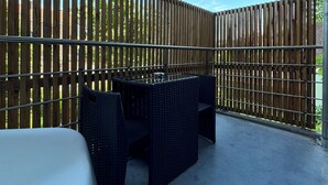 A covered patio with a metal railing, wicker furniture, and a concrete floor.