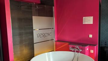 Un baño moderno con una bañera independiente, cabina de ducha con paredes de vidrio y una pared de acento en color rosa.