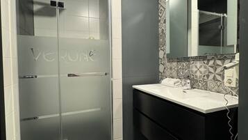Un baño moderno con ducha envuelta en vidrio, un lavamanos blanco y un mueble de tocador oscuro.