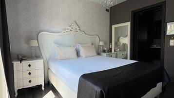 A bedroom with a large bed, white nightstands, a chandelier, and a dark wooden floor.