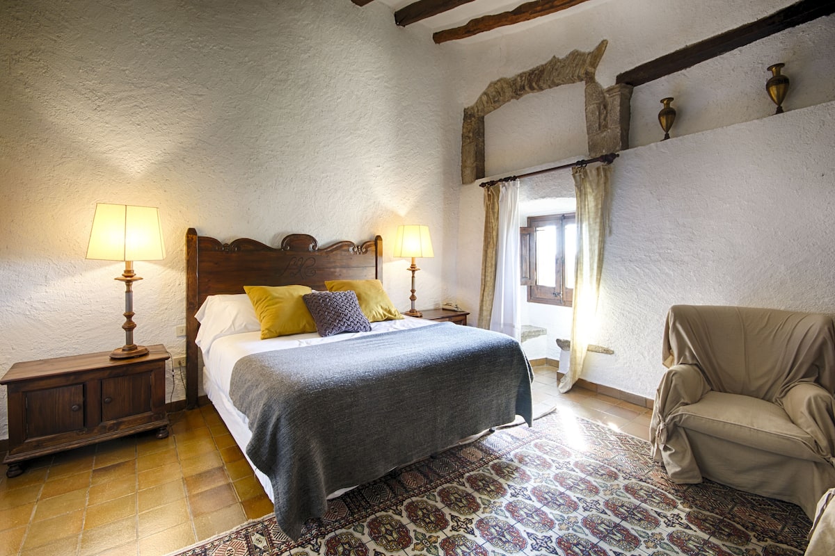 A bedroom with a wooden bed, two bedside lamps, a patterned rug, and a chair.
