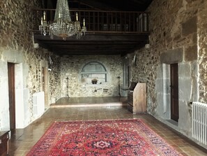 Una habitación con paredes de piedra, piso de madera, una araña y un tapete rojo con estampado.