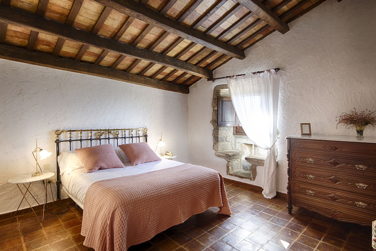 A bedroom with a bed, bedside table, dresser, and a stone wall.