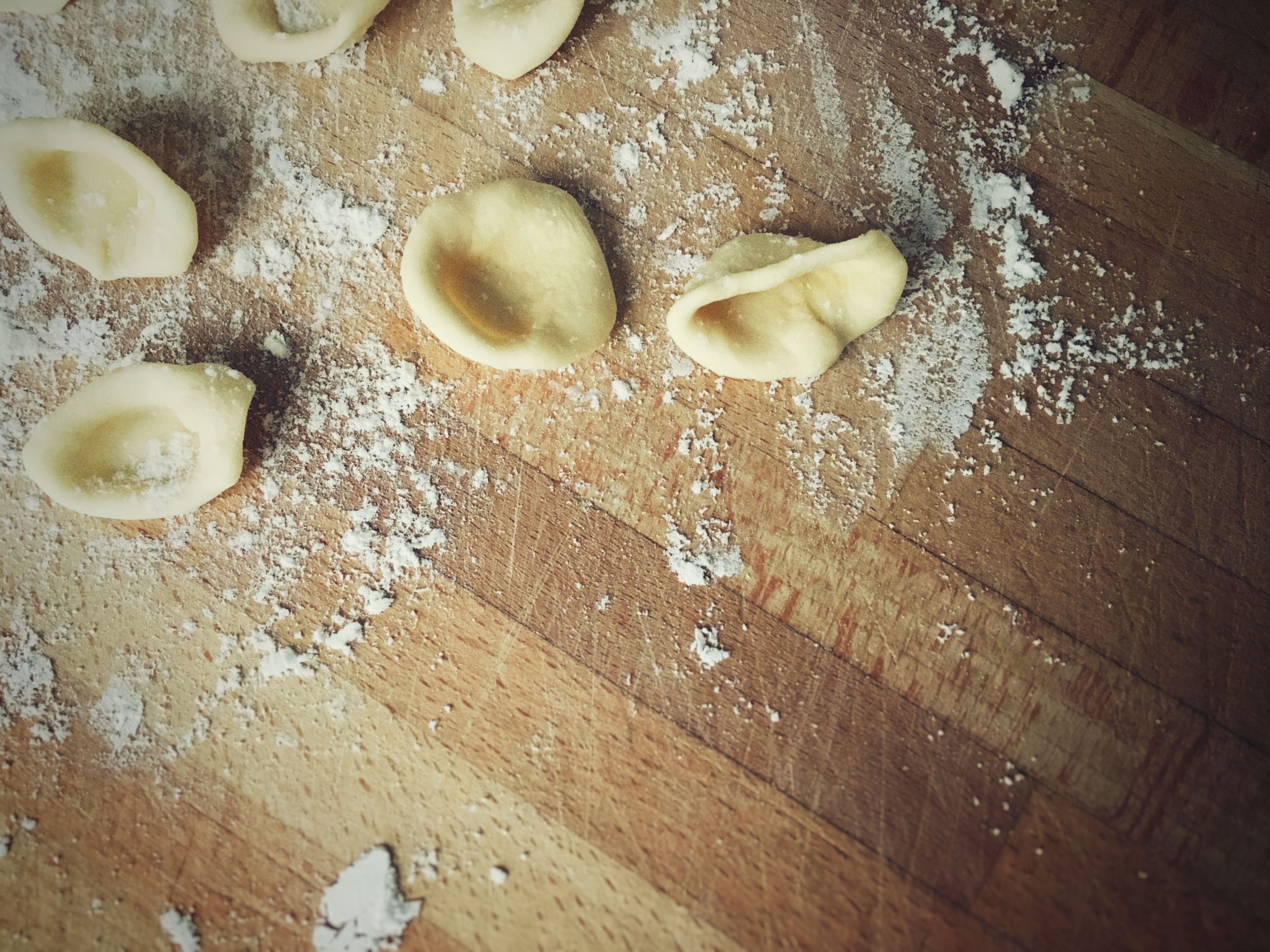 A wooden surface with flour and uncooked pasta shapes.