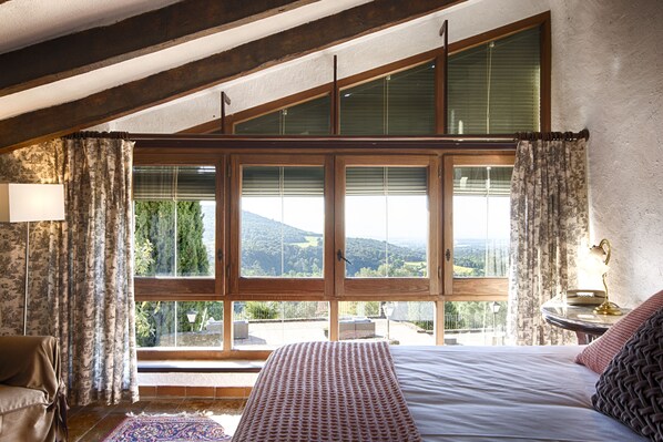 Een slaapkamer met een groot raam, een bed, een lamp en uitzicht op de omgeving.