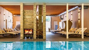 Een wellnessruimte met een stenen openhaard, lounge fauteuils en een zwembad.