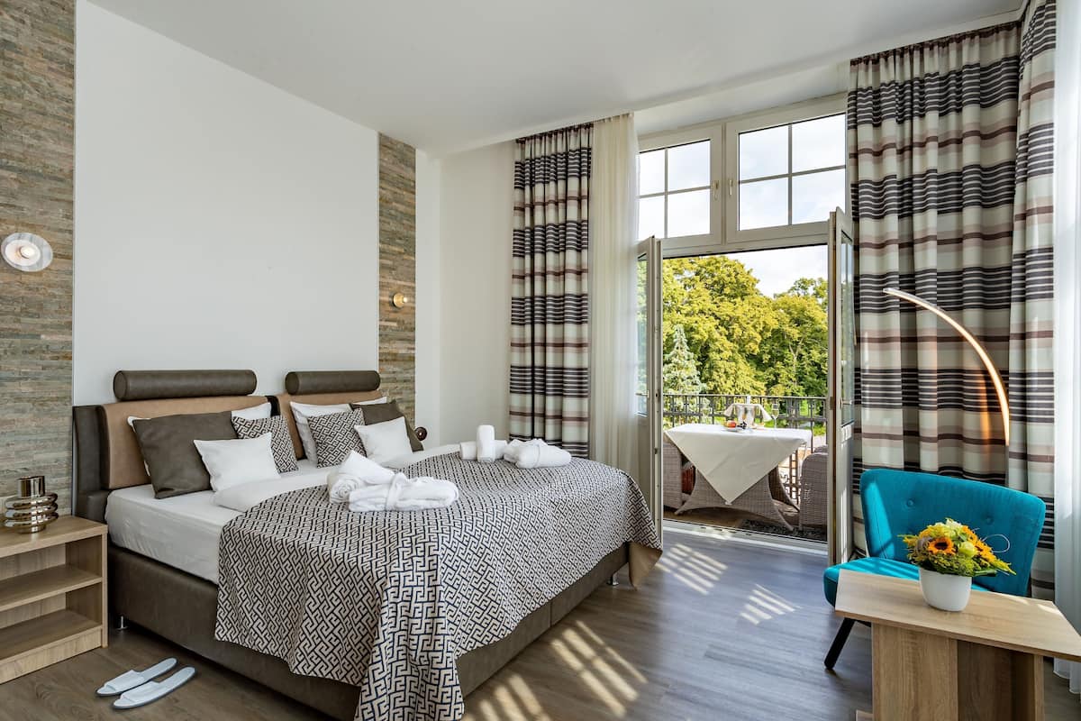 Une chambre d’hôtel moderne avec un grand lit, un balcon avec une table et un fauteuil bleu.