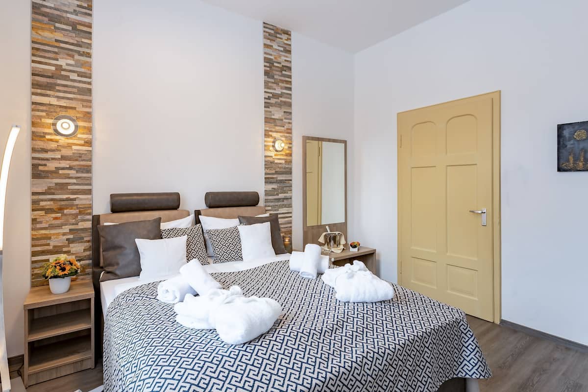 Une chambre d’hôtel avec un grand lit, une table de chevet avec une lampe, un miroir et une porte en bois.