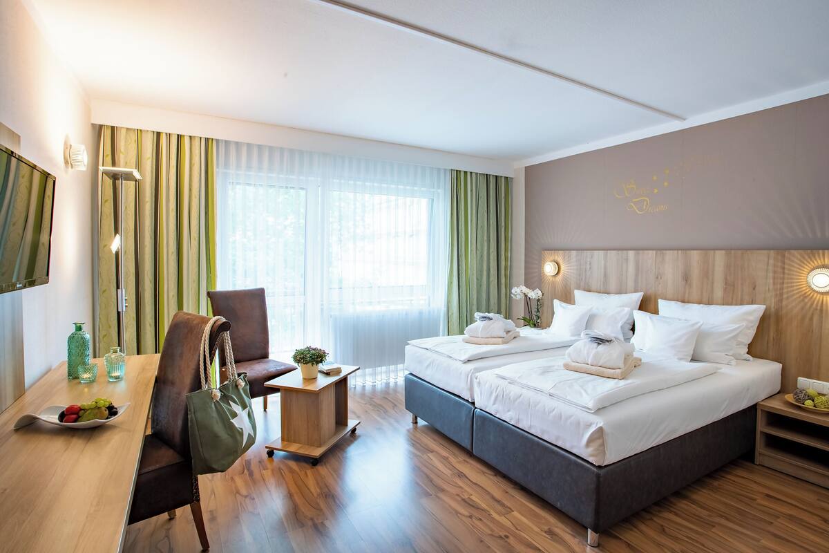 Ein Hotelzimmer mit Bett, Schreibtisch, Stuhl, Obst auf einem Tisch und einer grünen Tasche.