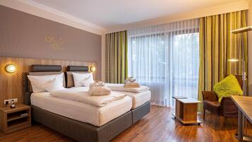 A hotel room with a double bed, bedside lamps, a wooden nightstand, a desk, a chair, and a large window with sheer curtains.