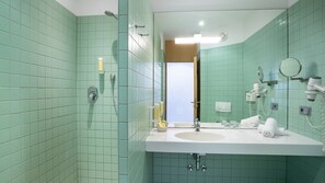 Een badkamer met groene tegels, een wastafel, een spiegel, een douche en een haardroger.