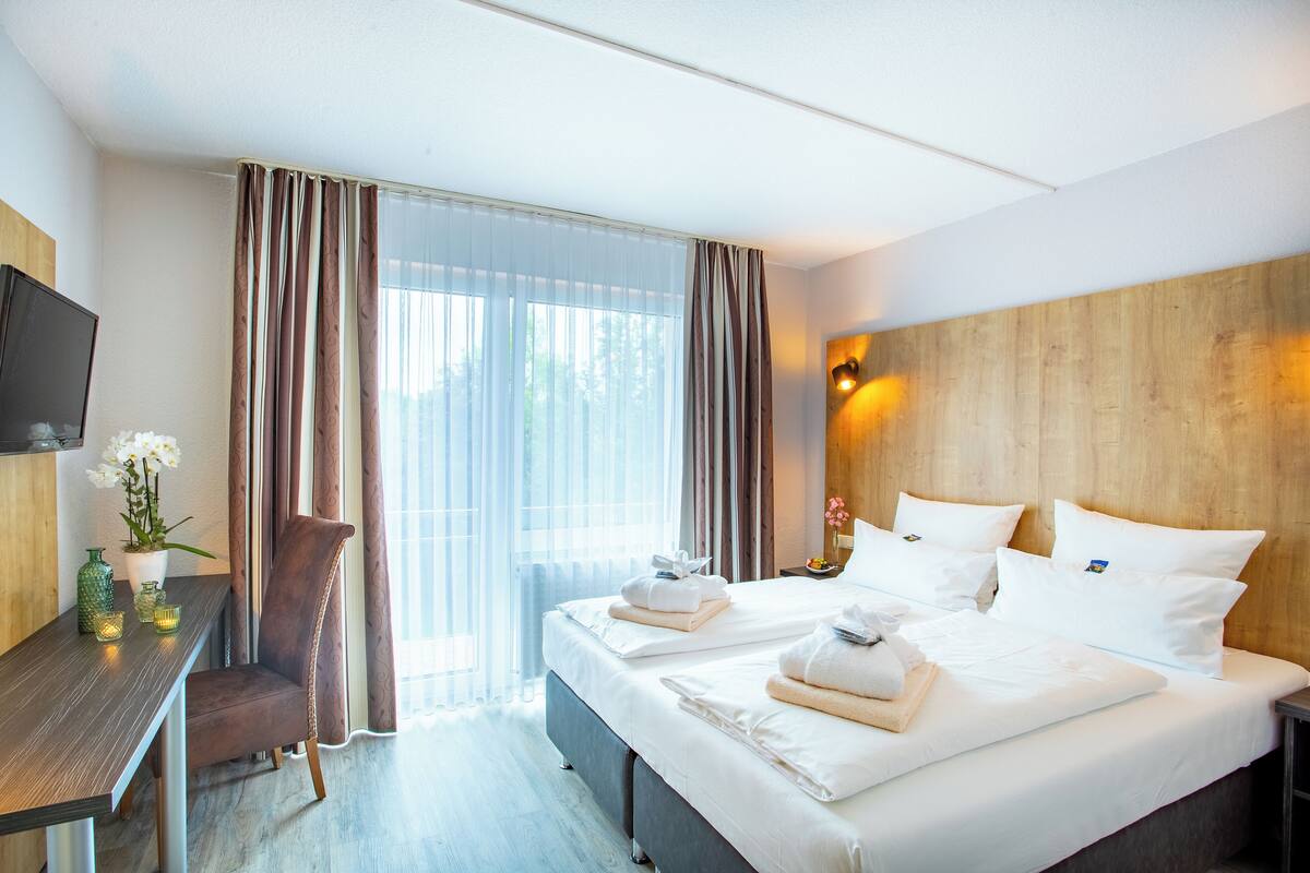 Ein Hotelzimmer mit Bett, Schreibtisch, Stuhl, Fernseher und einem Fenster mit Vorhängen.