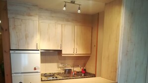 Una cocina compacta con armarios de madera, un refrigerador empotrado, una encimera con fregadero y dos taburetes.