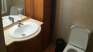 Un baño pequeño con lavamanos, espejo, armario de madera, inodoro y un cubo de basura.