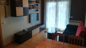 Un espacio habitable compacto con kitchenette, comedor y televisor montado en la pared.
