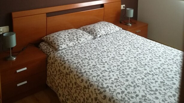 Un dormitorio con cabecera de madera, colcha estampada, dos mesitas de noche con lámparas y una lámpara de techo.