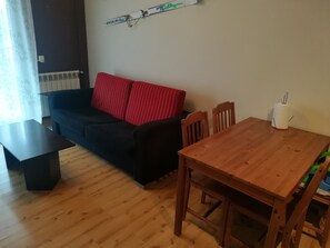 En stue med en mørk sofa, røde puder, et træsofabord og et spisebord med stole.