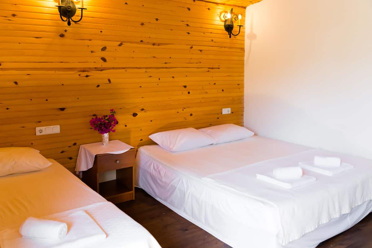 Habitación de hotel con dos camas, paneles de madera en las paredes y una mesita de noche con un jarrón de flores.