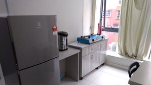 A compact kitchen with a refrigerator, a gas stove, and a microwave on the countertop. - My Homie Hotel PJ (Petaling Jaya)