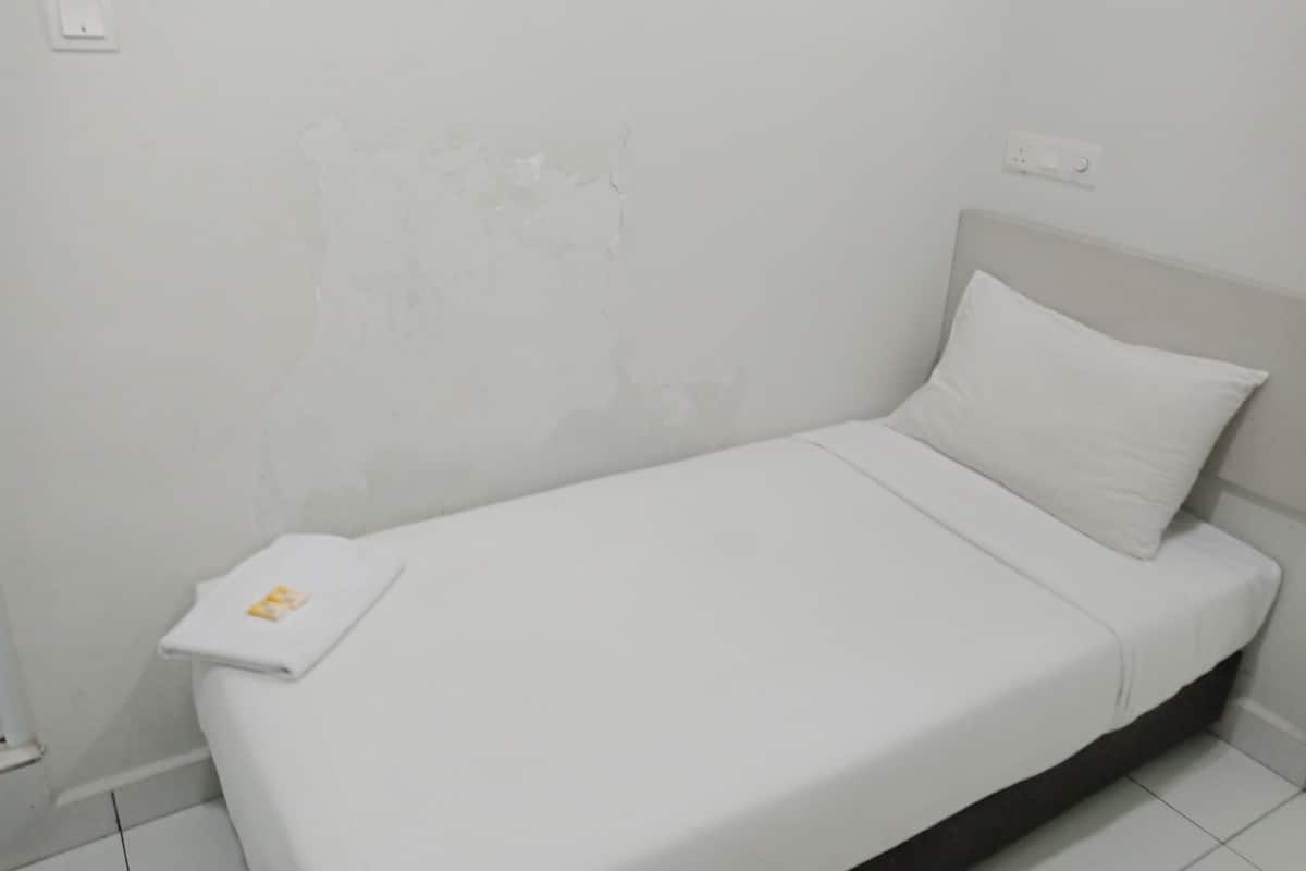 A small, white, single-bed room with a plain white wall and a simple, modern design.