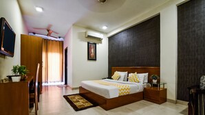 A bedroom with a bed, bedside tables, a desk, a chair, a potted plant, and a window with curtains.