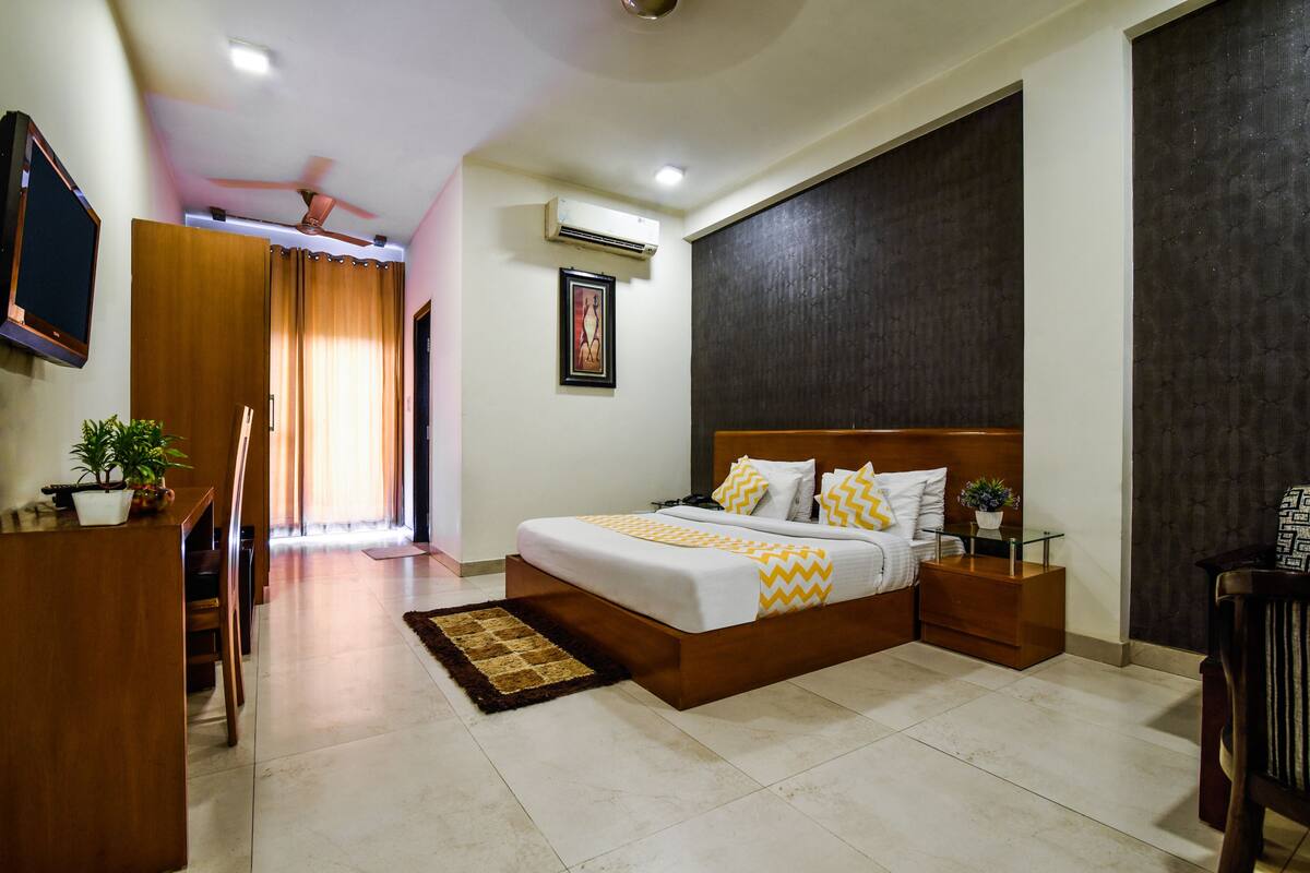 A bedroom with a bed, bedside tables, a desk, a chair, a potted plant, and a window with curtains.