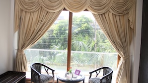 A balcony with two chairs, a small table, and a view of greenery through sheer curtains.