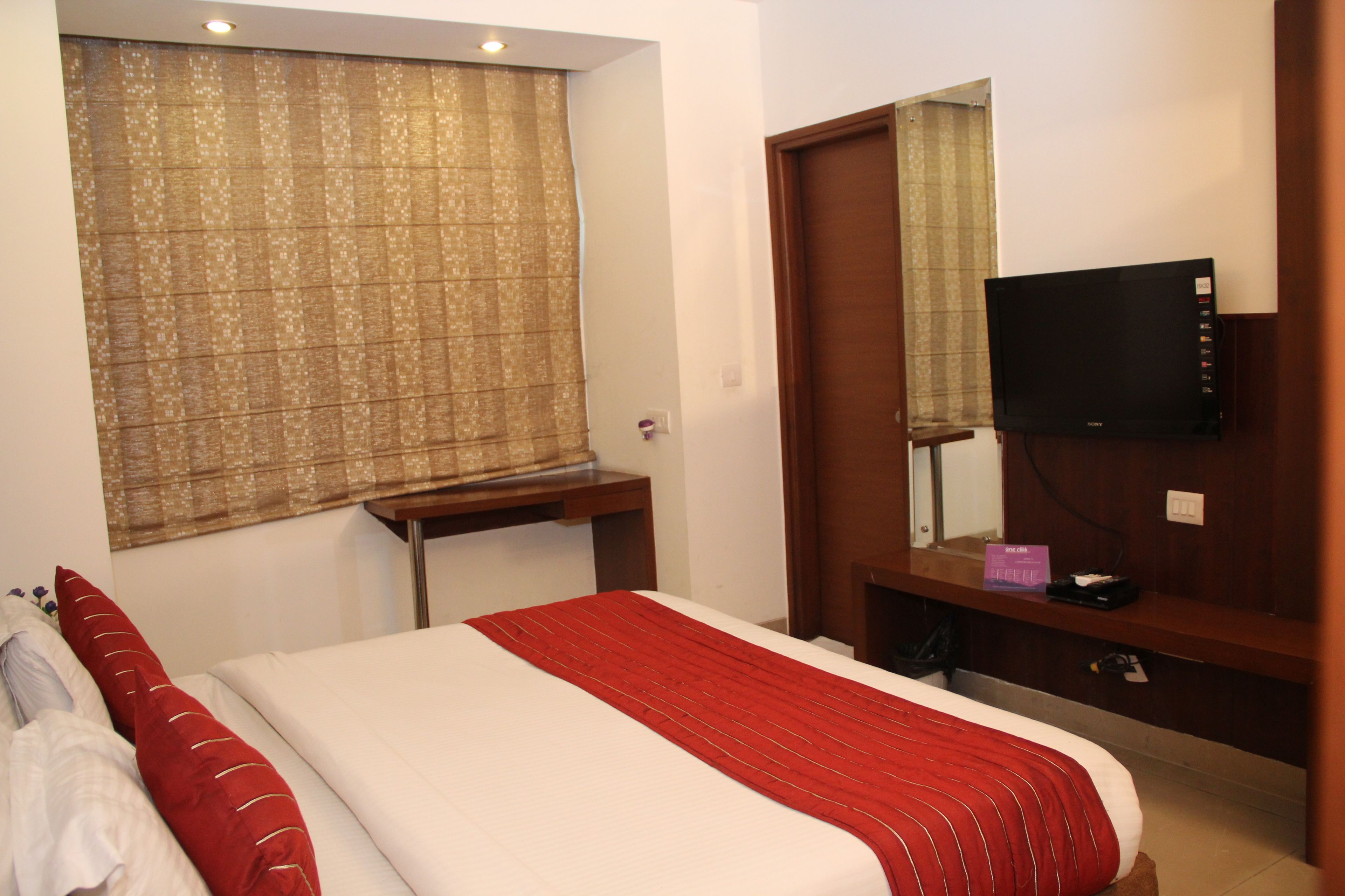 A hotel room with a bed, a TV, a desk, and a window with curtains.