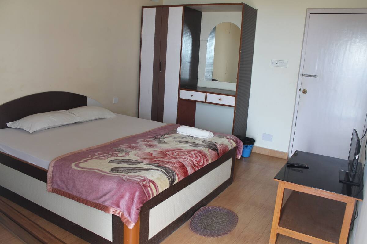 A bedroom with a bed, a bedside table, a dresser, a mirror, and a door.