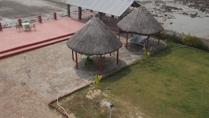 Um pavilhão à beira-mar com telhado de metal e estruturas de palha, rodeado por um calçadão e áreas de estar.