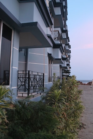A modern hotel with multiple balconies, a paved walkway, and lush greenery. - Arya Beach Resort (Kanthi)