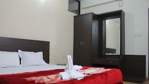 Quarto de hotel com uma cama, um cobertor vermelho, almofadas brancas, um guarda-roupa de madeira escura e um espelho.