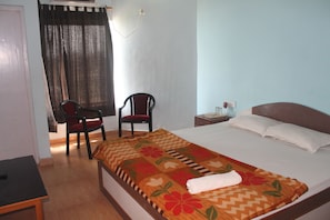 Une chambre d’hôtel avec un lit, deux chaises, une table de chevet et une fenêtre avec des rideaux.