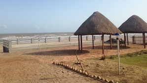 Uma praia com construções de palha, um caminho de areia e vista para o oceano.