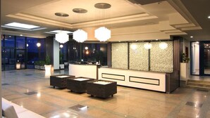 Een moderne lobby met een receptiebalie, een zithoek en grote ramen.