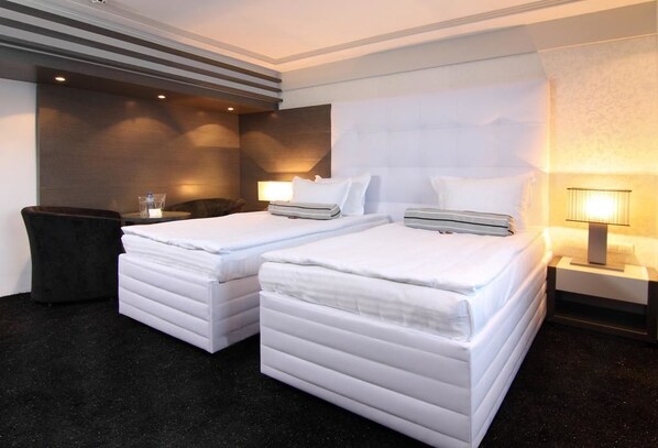 A hotel room with two beds, a dark carpet, a nightstand with a lamp, and a wall with a textured pattern.