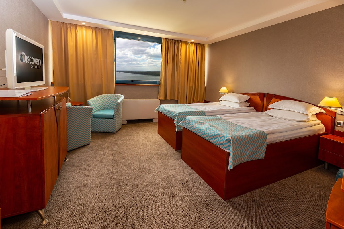 A hotel room with a bed, a desk with a computer, a chair, and a window with curtains.