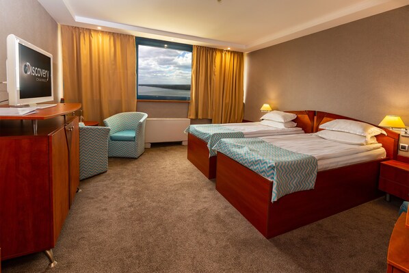 A hotel room with a bed, a desk with a computer, a chair, and a window with curtains.