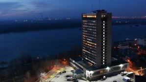 Een hoog hotel met meerdere verdiepingen, een parkeerplaats en uitzicht op een rivier in de schemering.