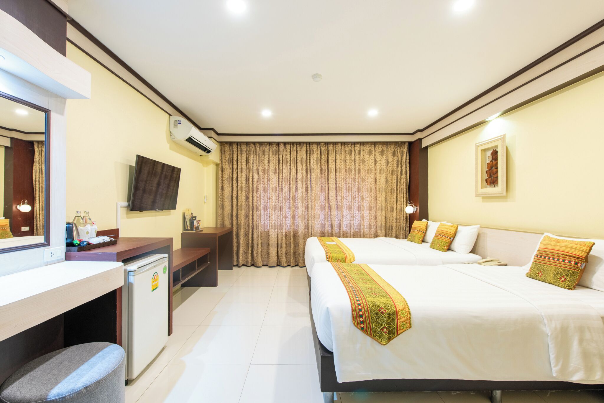 A hotel room with two beds, a desk, a television, and an air conditioning unit.