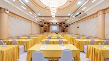 A conference room with multiple tables, chairs, and a large screen at the front.