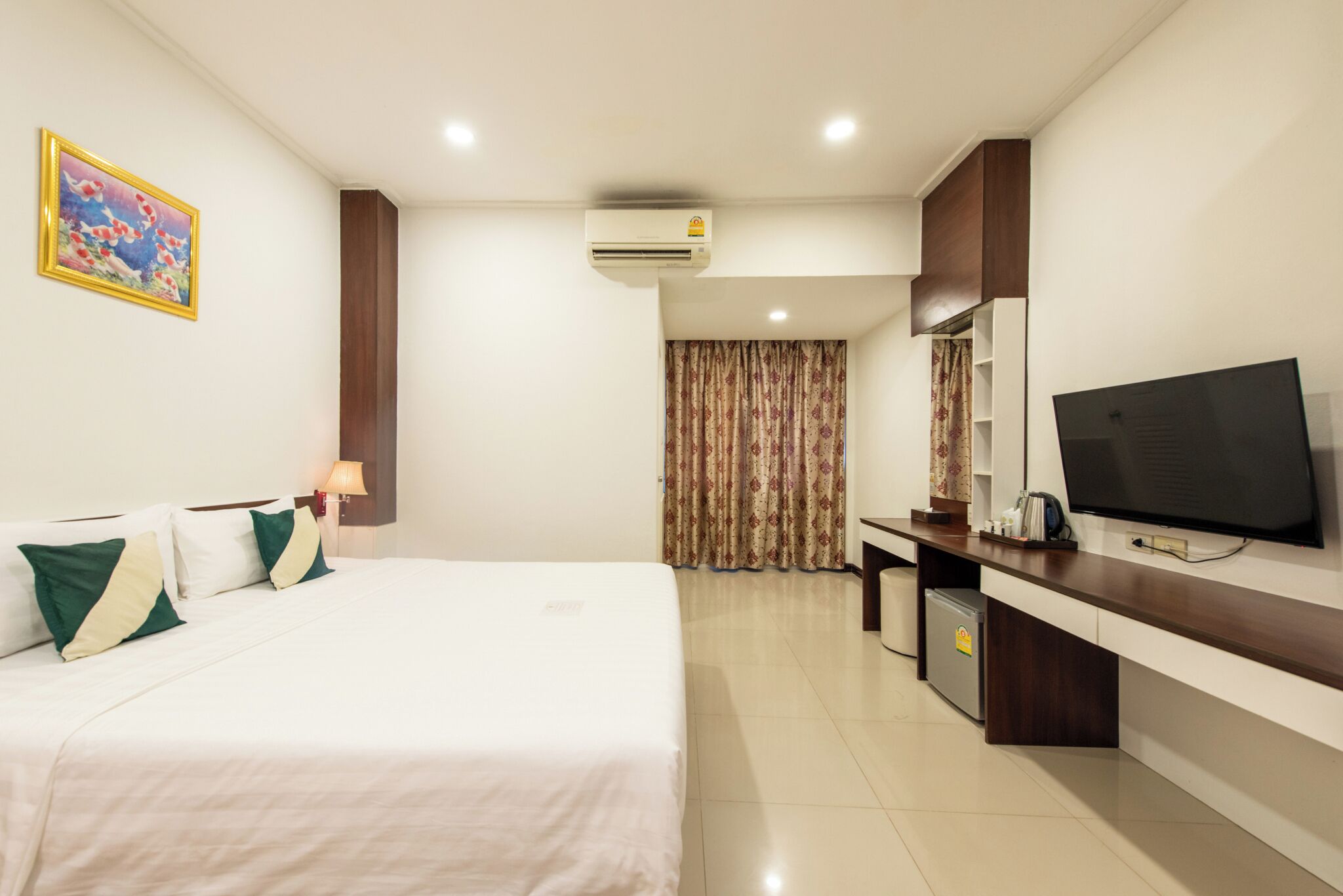 A hotel room with a bed, a desk, a television, and an air conditioning unit.