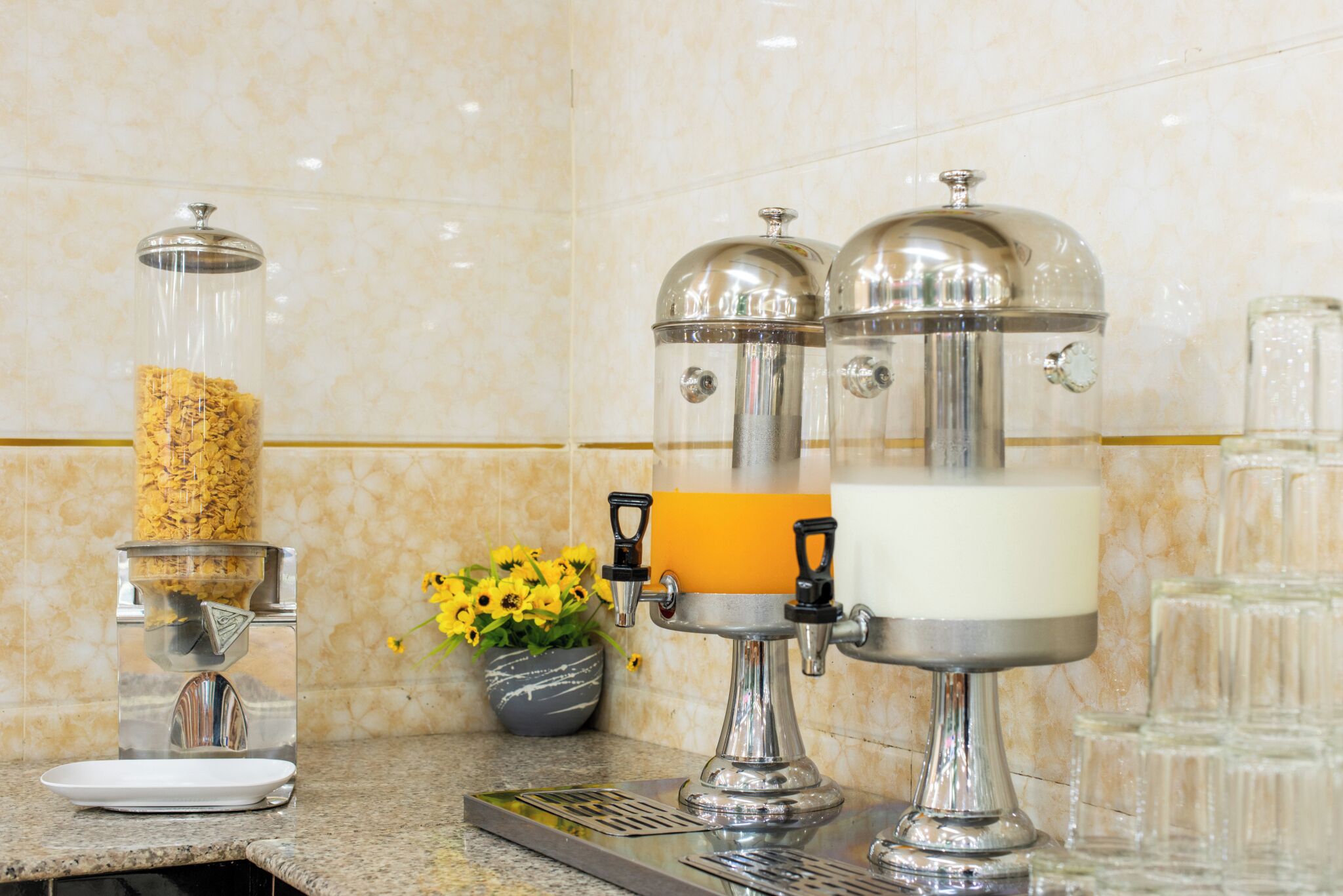 A coffee station with a coffee grinder, a milk frother, and a glass container with coffee grounds.