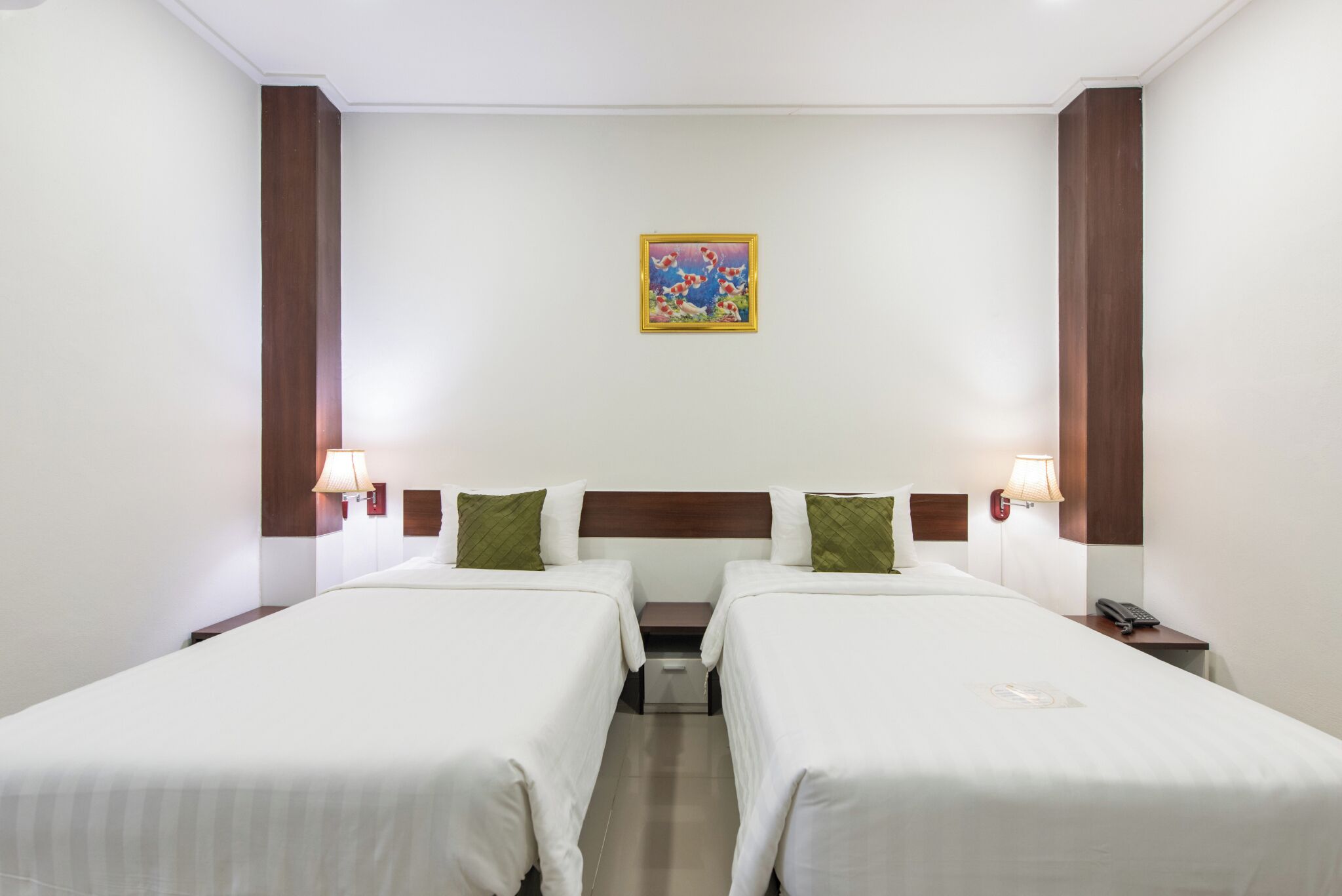 A hotel room with two beds, a nightstand with a lamp, a small table, and a painting on the wall.