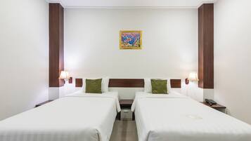 A hotel room with two beds, a nightstand with a lamp, a small table, and a painting on the wall.