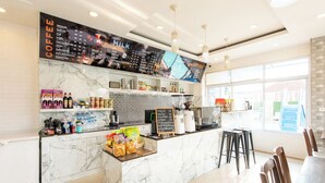 Una cafetería moderna con una barra de mármol, un menú en la pizarra y un área de estar con sillas y mesas.