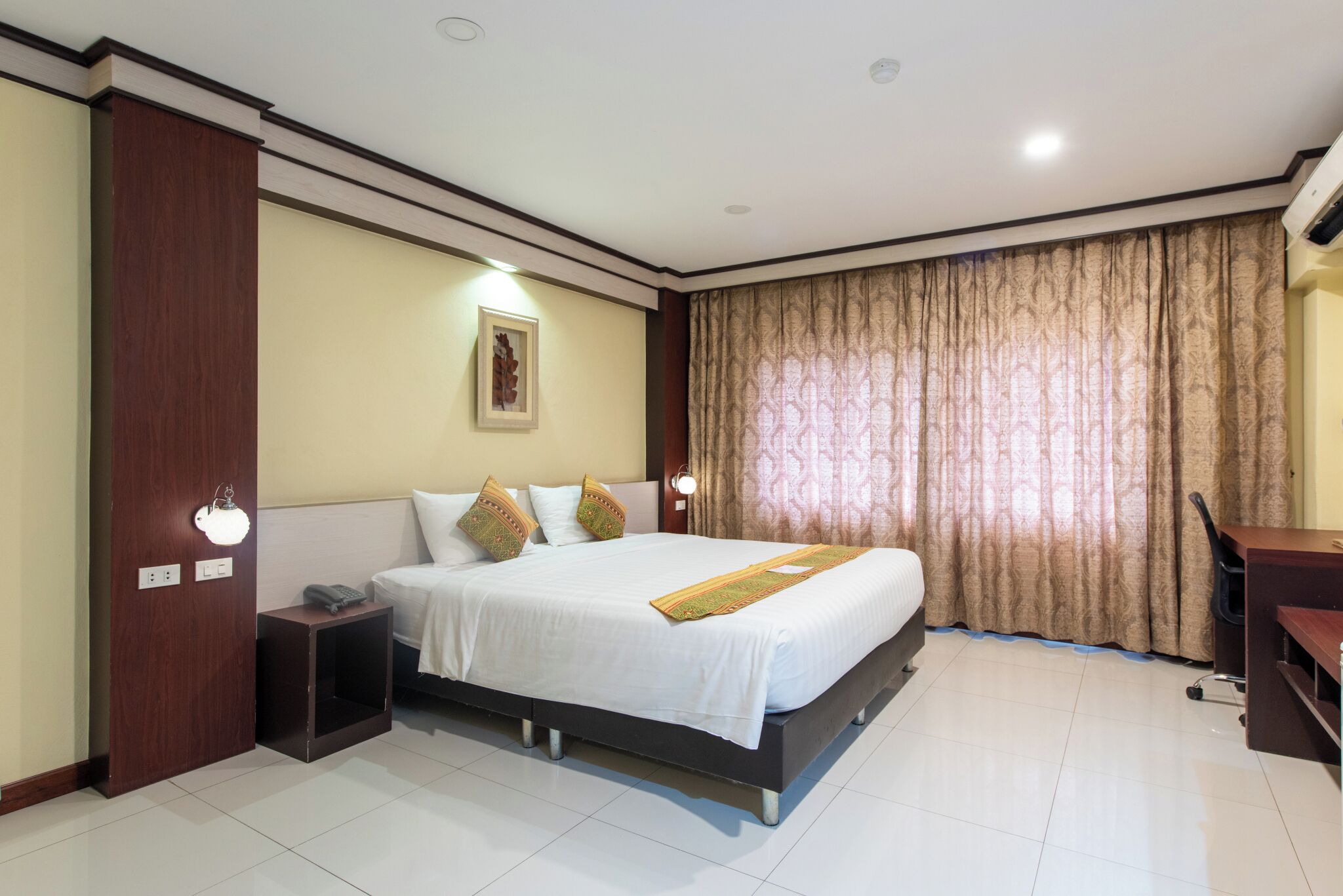 Quarto de hotel com cama grande, mesas de cabeceira, escrivaninha e cortinas.