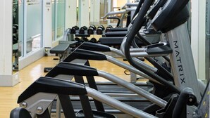 Un gimnasio con cintas de correr, espejos y un televisor en la pared.
